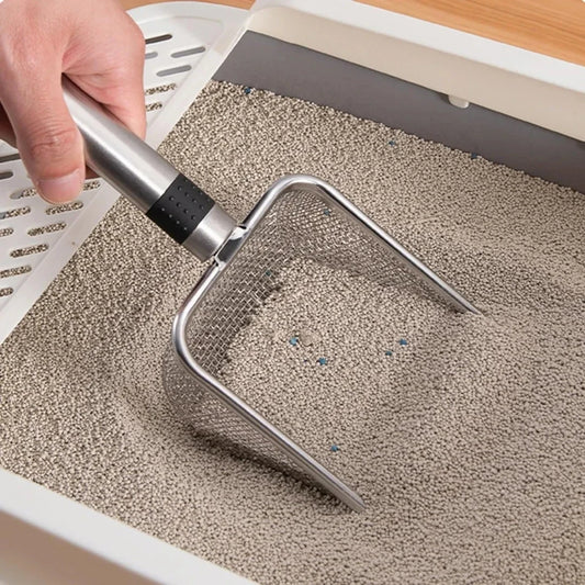 Hand holding stainless steel litter shovel over cat litter tray close up